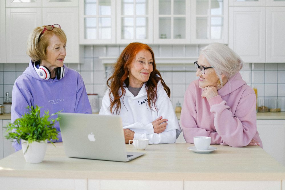 Cheerful aged women friends communicating while sitting at table at home